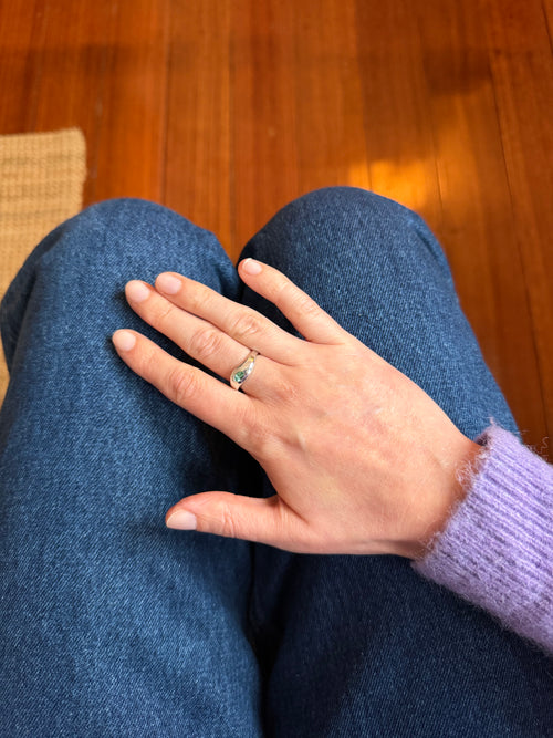 A silver rounded ring on a persons hand, resting on blue jeans with a light purple sweater