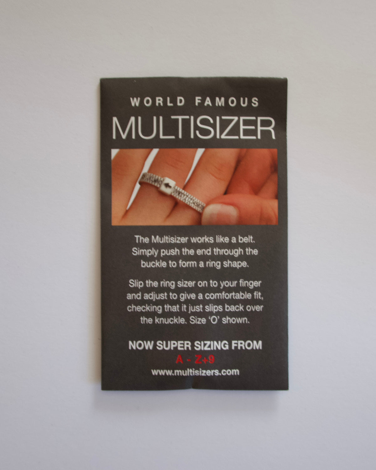 A rectangular black card for the 'World Famous Multisizer' by MultiShapers, featuring white text, a photo of hands using the device, and instructions on how to form a ring, shown against a plain light gray background.