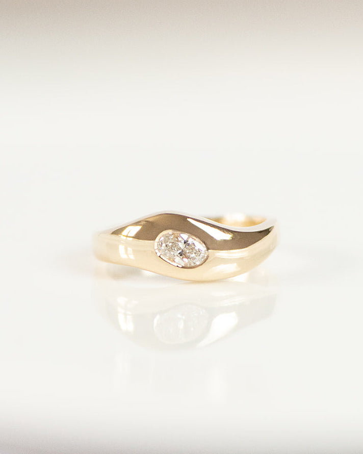 A gold ring with a small clear white diamond, resting on a white reflective surface.