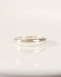 A minimalist polished silver band ring resting on a white ceramic plate with a soft reflection.